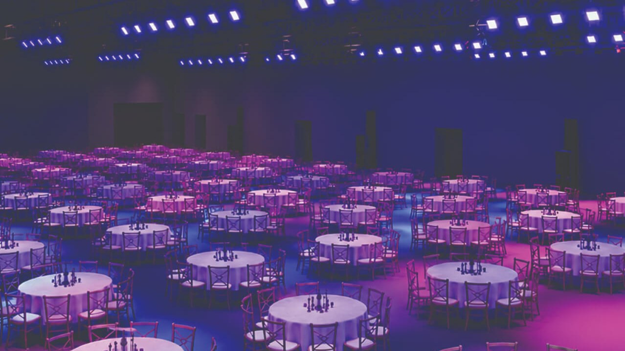 Conceptual rendering of the 19,000 sq. ft. convention space at Universal Epic Universe set for a banquet with round tables under purple and blue lighting